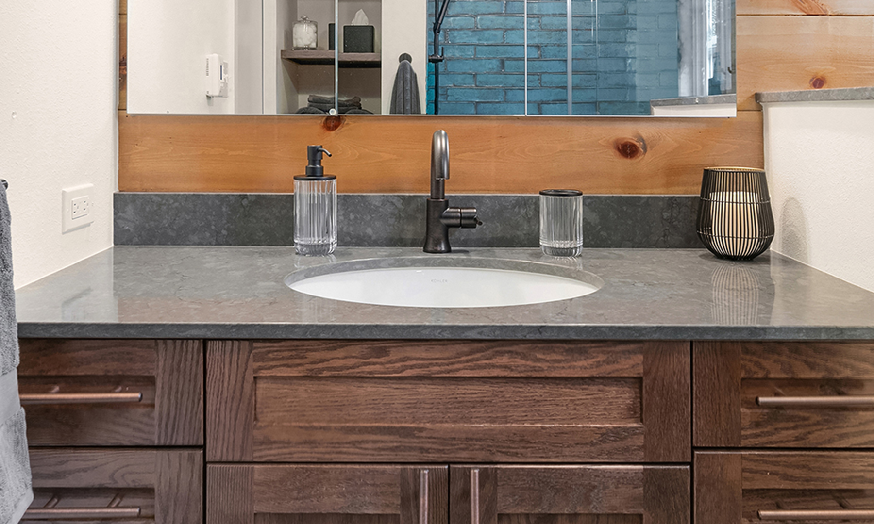 Undermount sink under a dark gray stone counter with aged bronze faucet and dark wood vanity and cladding walls