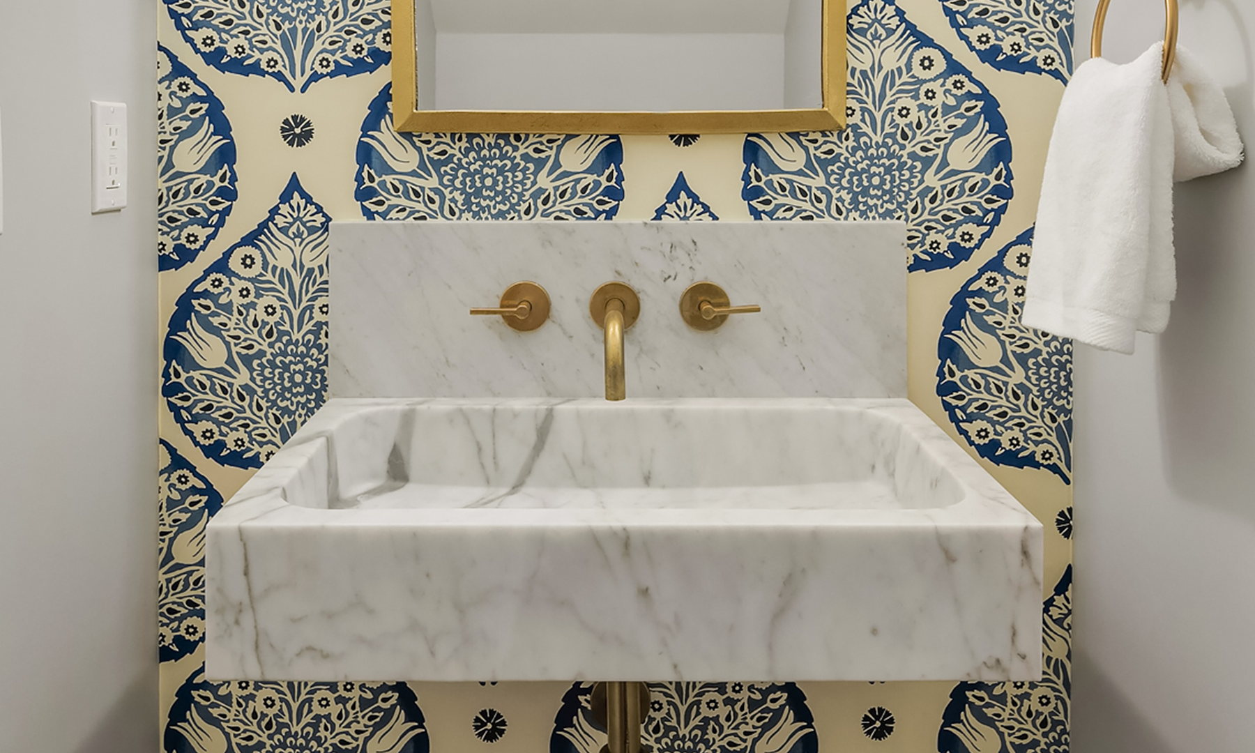 Marble wall mounted sink with satin bronze faucet and floral wallpaper